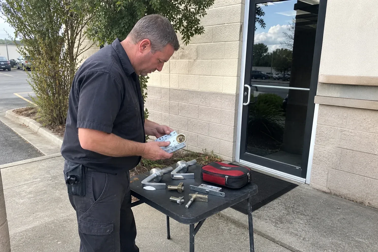 Technician examining detached commercial lock hardware on a table outside a shop entrance. — Business Lockout Service, Woodstock
