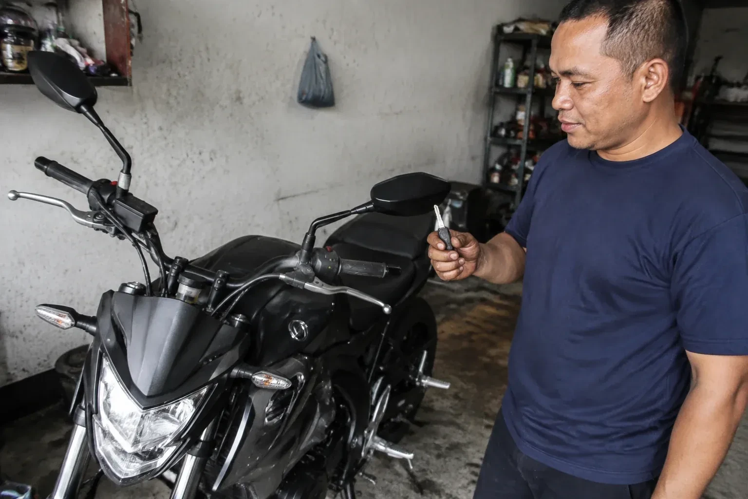 Person holding a key beside a black motorcycle in a garage. — Motorcycle & Scooter Keys, Woodstock